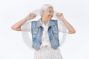 Carefree, happy, lively joyful senior woman with grey hai, raising hands up, fist pump or stretching feeling cheerful