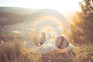 Carefree happy woman lying on green grass meadow on top of mountain edge cliff enjoying sun on her face. Enjoying nature sunset