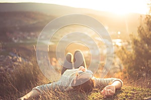 Carefree happy woman lying on green grass meadow on top of mountain edge cliff enjoying sun on her face. Enjoying nature sunset