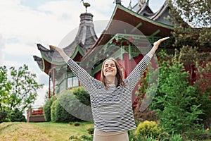 Carefree happy woman in spring or summer park raising arms with happiness, caucasian girl relaxing and enjoying life on nature