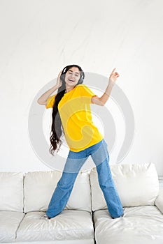 Carefree happy young woman in headphones dancing on couch in modern minimal living room.