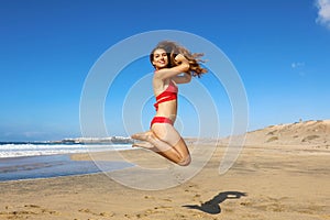 Carefree healthy bikini woman jumping on the beach. Happy smiling girl doing a jump of freedom and happiness in a free body on