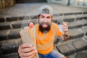 Carefree hipster eat junk food while sit on stairs. Hungry man snack. Junk food. Guy eating hot dog. Man bearded bite