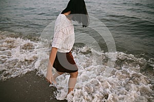 Carefree hipster woman walking barefoot in sea waves on beach. Feet in water foam. Mindfulness