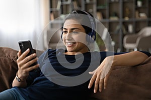 Carefree indian lady wearing headset listen to music from cell