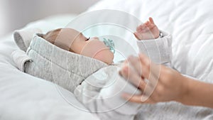 Carefree little baby with nipple sleeping on white bed during mother hand caress his arm close-up