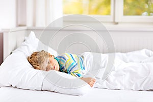 Carefree little kid boy sleeping in bed in colorful nightwear. photo
