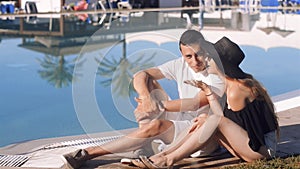 Carefree lovers resting near swimming pool. Girl in sunglasses and hat. Couple on vacation, sunbathing, relaxing. Vacation, touris
