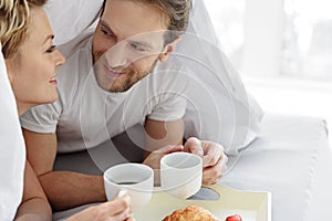 Carefree man and woman enjoying coffee in bedroom