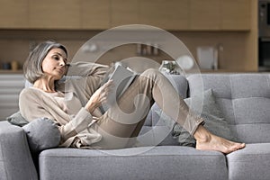 Carefree mature woman resting no sofa with favourite book