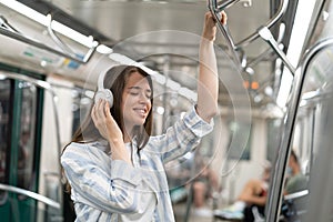 Carefree millennial cute girl passenger listening to music with wireless earphones in subway train.