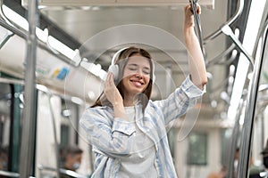 Carefree millennial cute girl passenger listening to music with wireless earphones in subway train.