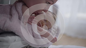 Carefree newborn baby sleeping in basket with woman kissing hand and cheek in slow motion. Side view happy loving mother