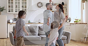 Carefree parents and cute children dancing having fun in kitchen