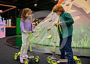 Carefree preschool children riding scooters together on indoor playground