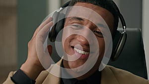 Carefree relaxed African American man happy businessman in headphones listen song dancing to music at office business