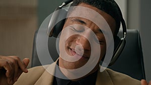 Carefree relaxed African American man happy businessman in headphones listen song dancing to music at office business