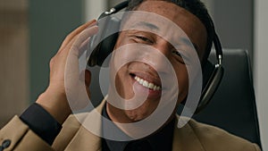 Carefree relaxed African American man happy businessman in headphones listen song dancing to music at office business