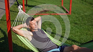 Carefree relaxed Caucasian man lying in hammock in sunshine outdoors. High angle view portrait of happy confident