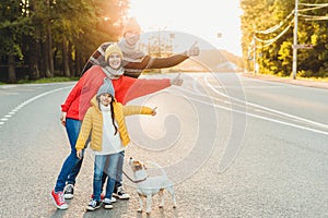 Carefree relaxed friendly family walk on road in countryside with dog, raise thumbs with enjoyment, wear warm clothes and sport sh
