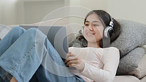 Carefree relaxed girl arabian hispanic student freelancer in headphones rest on sofa talk at web camera computer listen