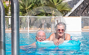 Carefree senior couple smile in the swimming pool looking at camera. Happy relaxed retired people enjoying summer vacation doing