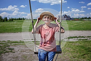 Carefree senior woman in straw hat swinging on a wooden swing, age beauty, baby boomer generation