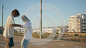 Carefree skaters holding hands riding longboards at evening. Teen pair together