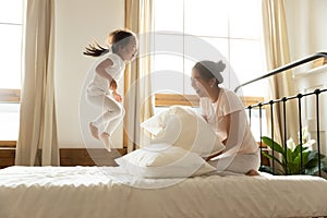 Carefree small daughter jump on bed while vietnamese mother laughing