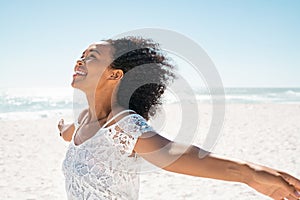 Carefree smiling black woman at beach outstretching arms