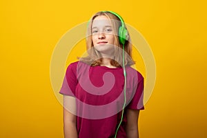 Carefree smiling young girl listens music in headphones isolated over vivid yellow background