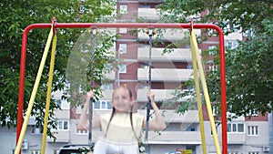 Carefree teenager girl swinging on playground in residential area on brick house background. Smiling girl on swing on