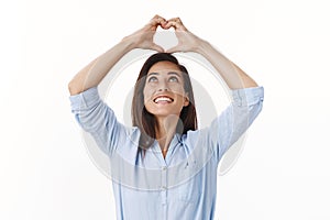 Carefree tender caucasian middle-aged woman, wife confess sympathy, raise hands show heart sign above head, smiling