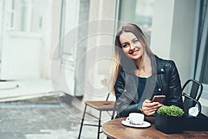 Carefree time in cafe. Attractive young woman with a smile sitting in cafe outdoor and typing quick message