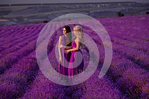 Carefree two beautiful women enjoying sunset in lavender field. Harmony. Attractive blond and brunette with long curly hair style