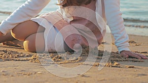 Carefree unrecognizable girl drawing a heart shape on the wet sand at exotic sunset