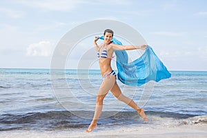 Carefree woman on a beach with a floating scarf