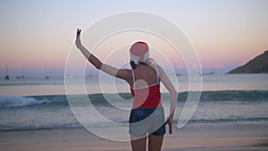 Carefree woman dancing and jumping happy in santa hat and red swimsuit at sunset on the tropical paradise beach