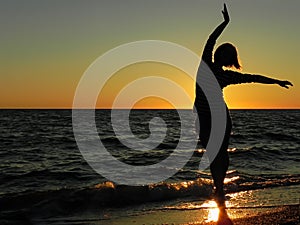 Carefree woman dancing in the sunset on the beach.