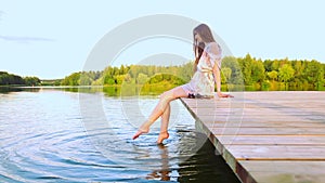 Carefree woman dangles her feet in the water while sitting on the pier