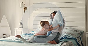 Carefree woman and little daughter fighting with pillows in bedroom