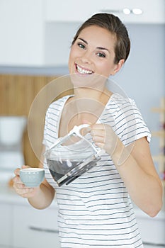 carefree woman pouring coffee from cafetiere jug into cup