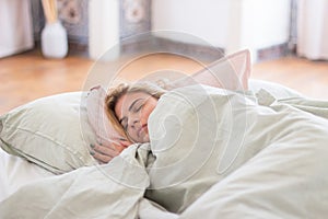 Carefree woman sleeping in bed under blanket