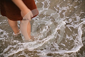 Carefree woman standing barefoot in sea waves on beach. Feet in water with foam, summer vacation