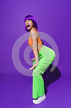 Carefree woman wearing colorful sportswear twerking against purple background