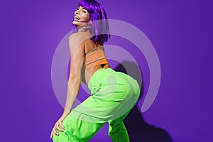 Carefree woman wearing colorful sportswear twerking against purple background