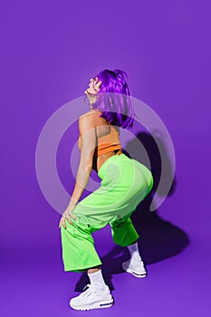 Carefree woman wearing colorful sportswear twerking against purple background