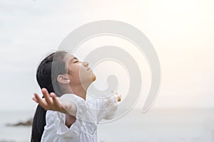 Carefree young Asian girl taking deep breath for natural blissful fresh air facing against sky, opening arms relaxing on the sea