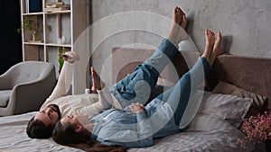 Carefree young Caucasian couple love enjoying relaxing lying in bed using phone smartphone gadget. Man and woman make