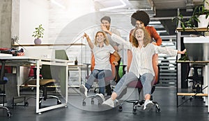 Carefree young colleagues having chair race competition in office
